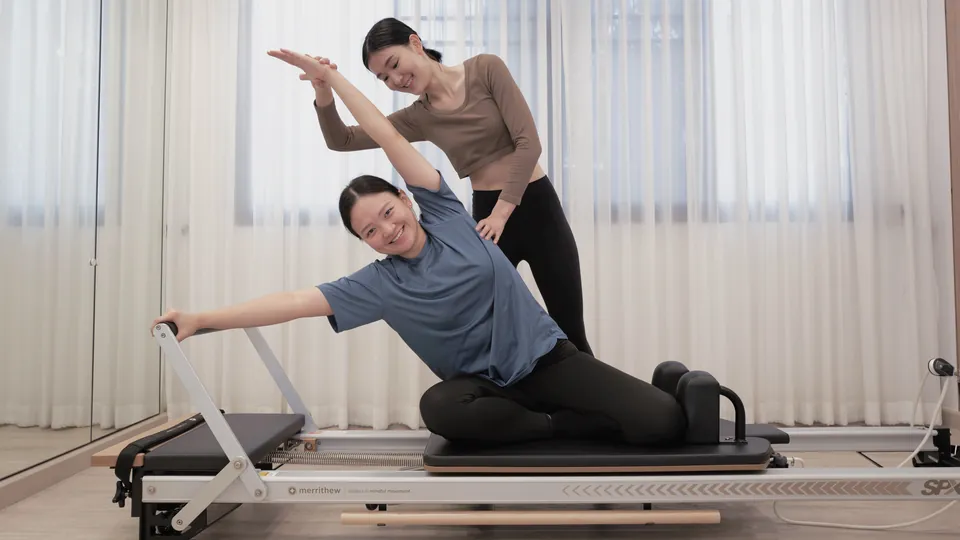 A Luna instructor guiding a client through a side bend on the reformer